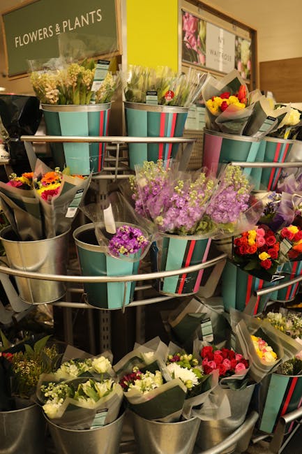 A display of various floral bouquets arranged in metal and striped turquoise buckets inside a flower shop. The bouquets feature a range of fresh flowers including purple statice, white roses, yellow a